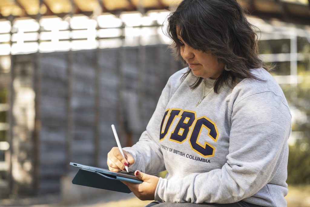 UBC student writing on an iPad, representing Indigenous youth empowerment through the Youth Grant.